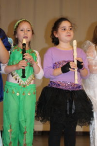 Students wearing costumes with a recorder on stage